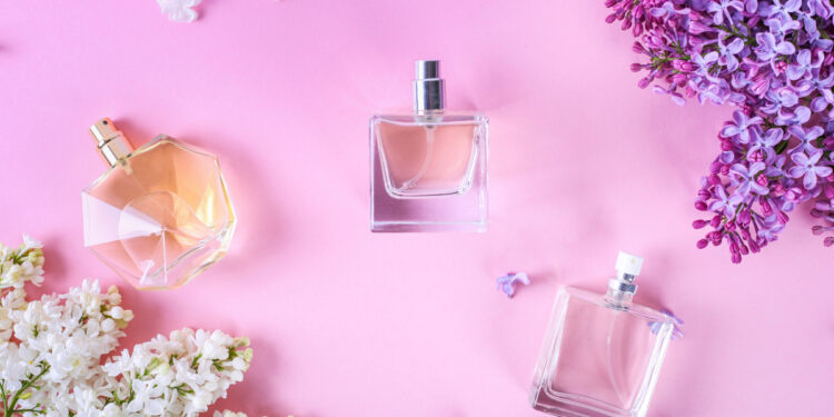 Butelki perfum na jednolitym tle w kompozycji z kwiatami